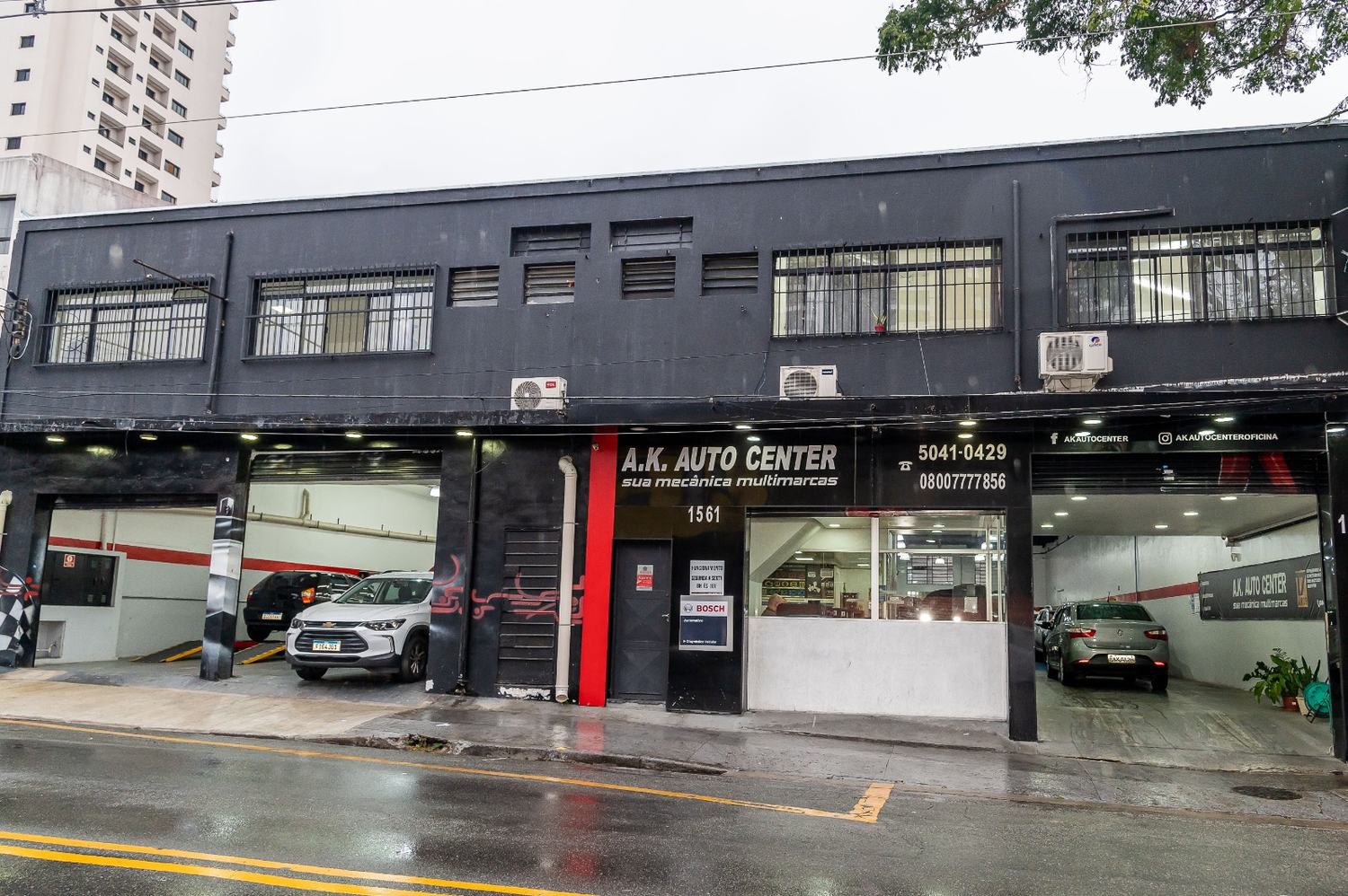 Fachada preta da A.K. Auto Center na rua Américo Brasiliense, com dois boxes abertos e carros dentro.