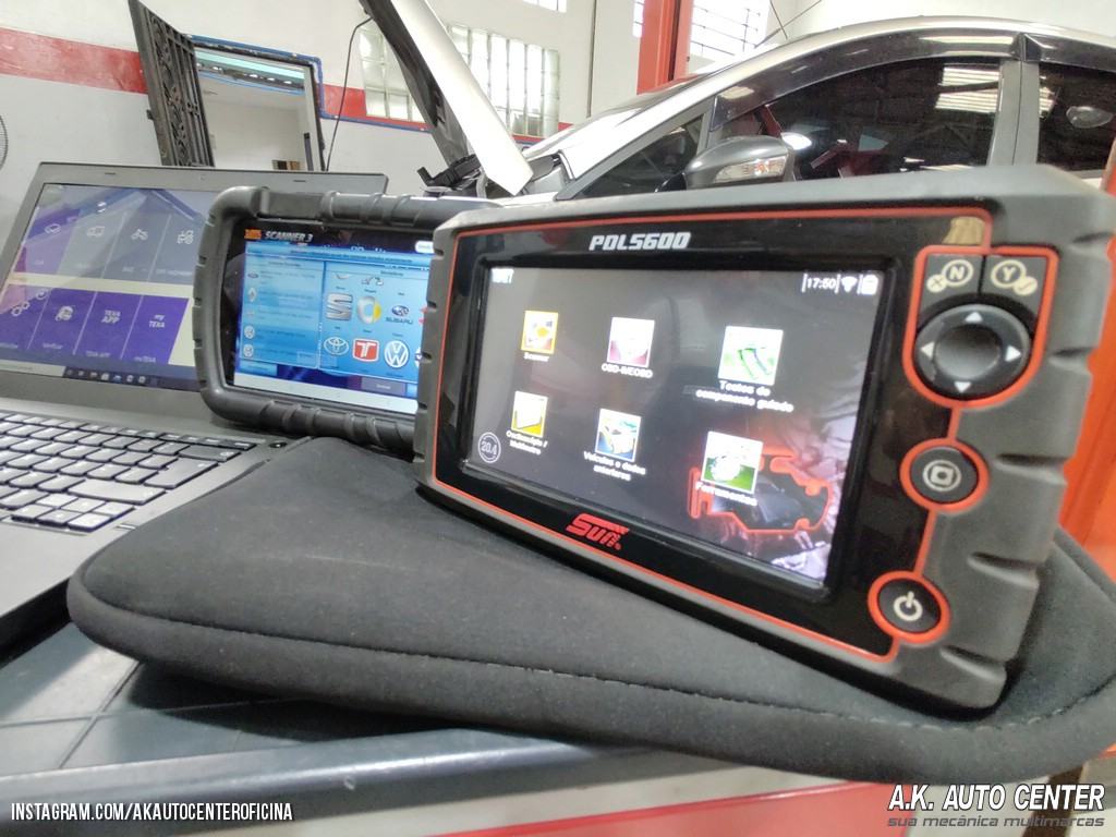 Scanner de diagnóstico automotivo apoiado sobre o carro, ao lado de um notebook com o programa de leitura aberto.